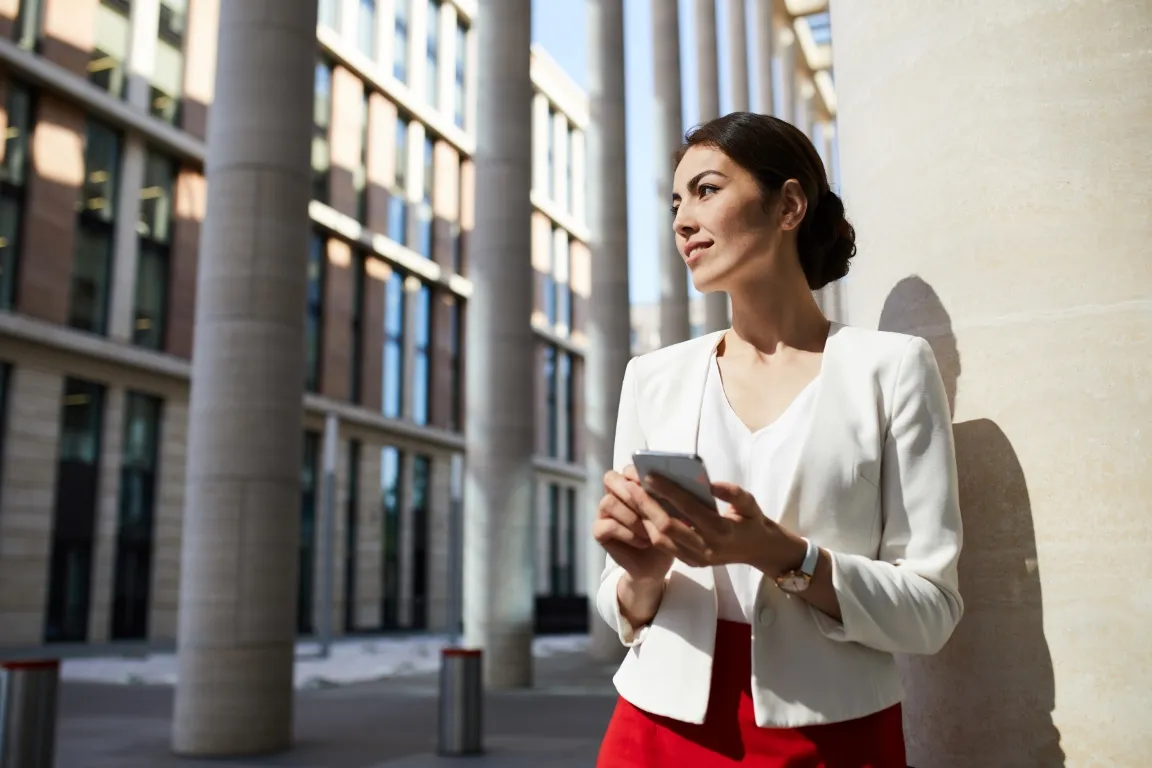 A woman strolling outside the city, with a blurred background, wearing a pensive yet smiling expression.