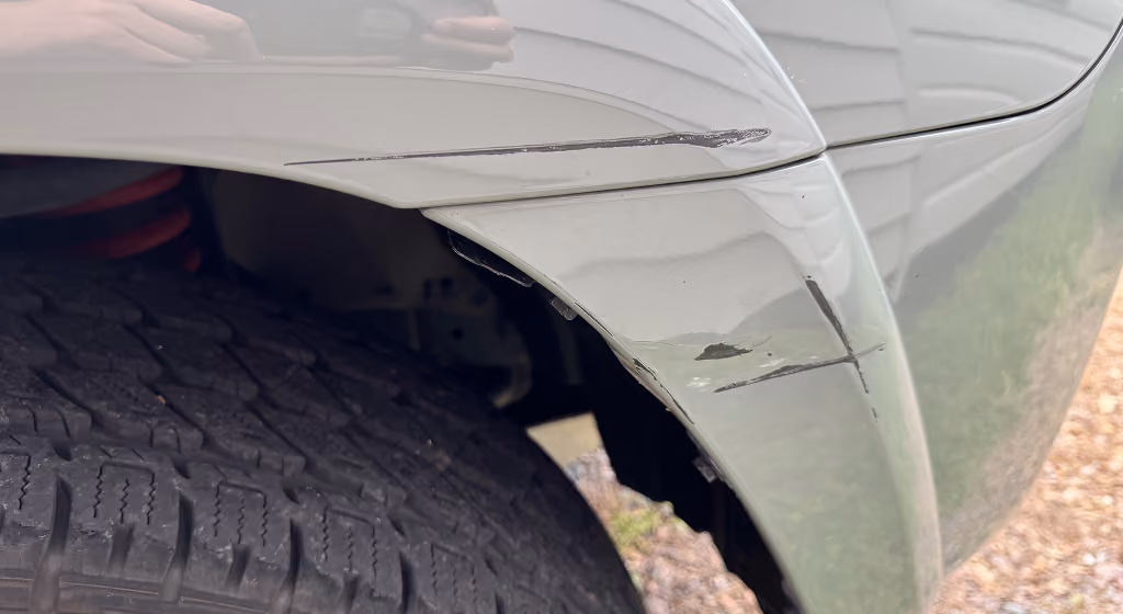 Close-up of car tire and scratched grey car fender with black scuff marks and paint damage.