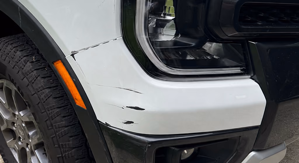 Close-up of white vehicle's front left fender with black scratches near the headlight and tire.