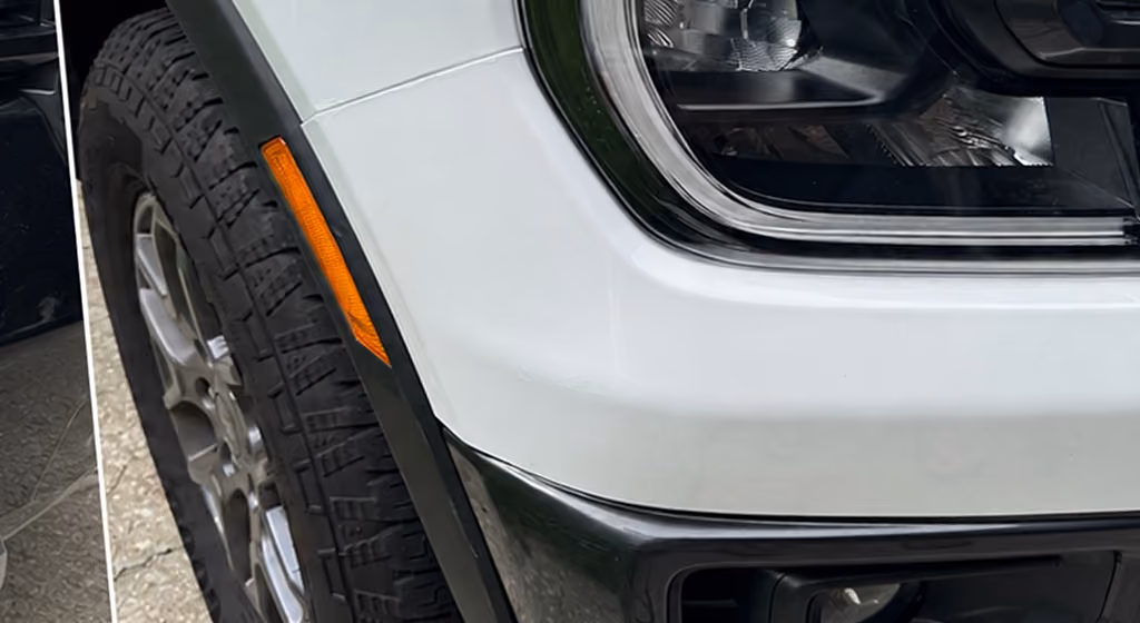 Close-up of a white vehicle's front tire, black fender, orange side marker, and headlight.