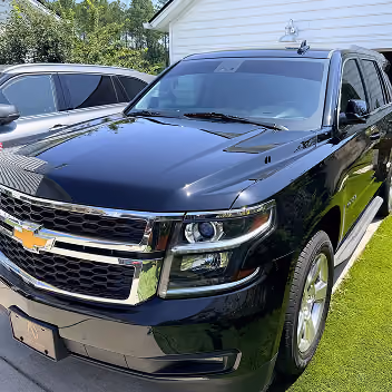 Black Chevrolet SUV parked on green grass beside another vehicle with a white building in the background.