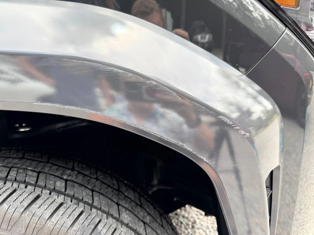 Close-up of a black car's fender with visible scratches and scuff marks above the tire.