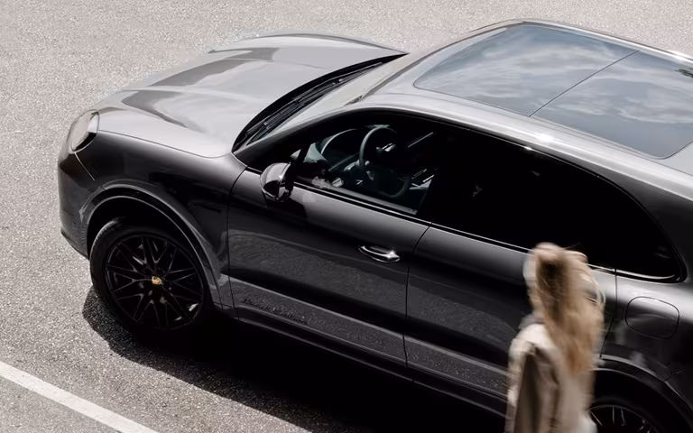 Porsche Cayenne negro visto desde arriba en un estacionamiento, con una persona caminando junto al auto