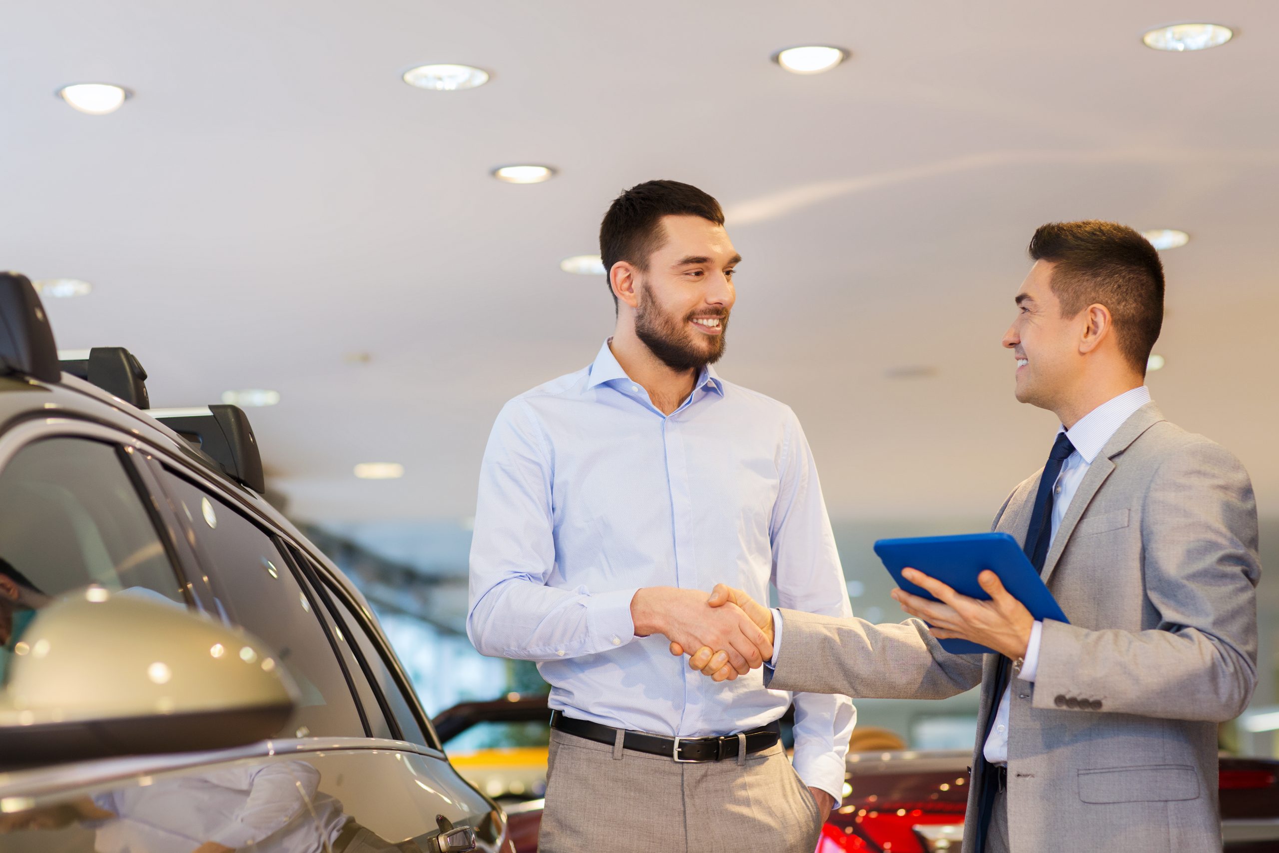 Vendedor de concesionario mostrando el catálogo online de autos a un cliente en una tablet