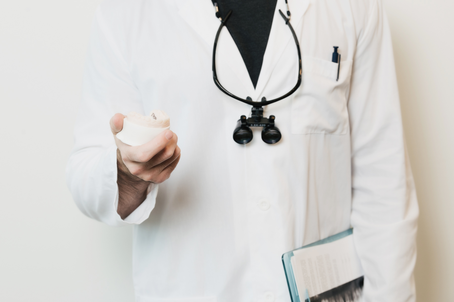 Dentist in a white coat with loupes around his neck holding a dental item