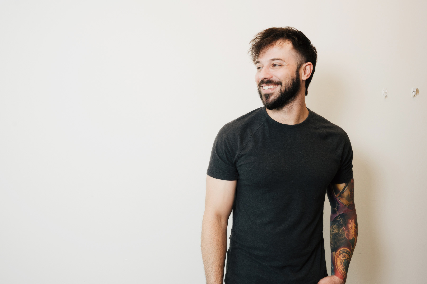 Smiling man with a tattoo sleeve standing against a white wall