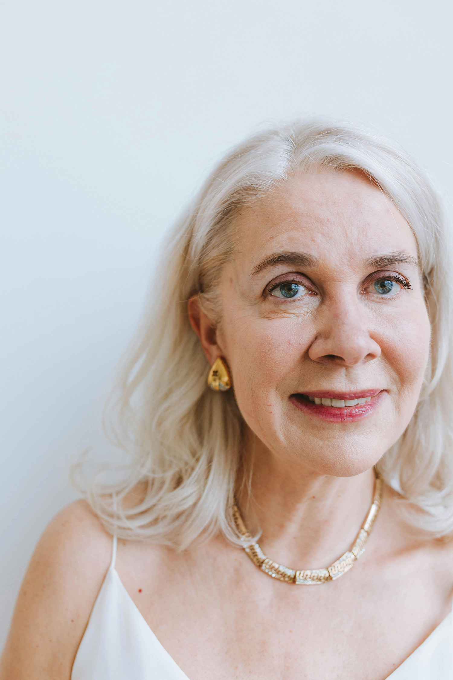 Portrait of a smiling older woman with white hair and gold jewelry