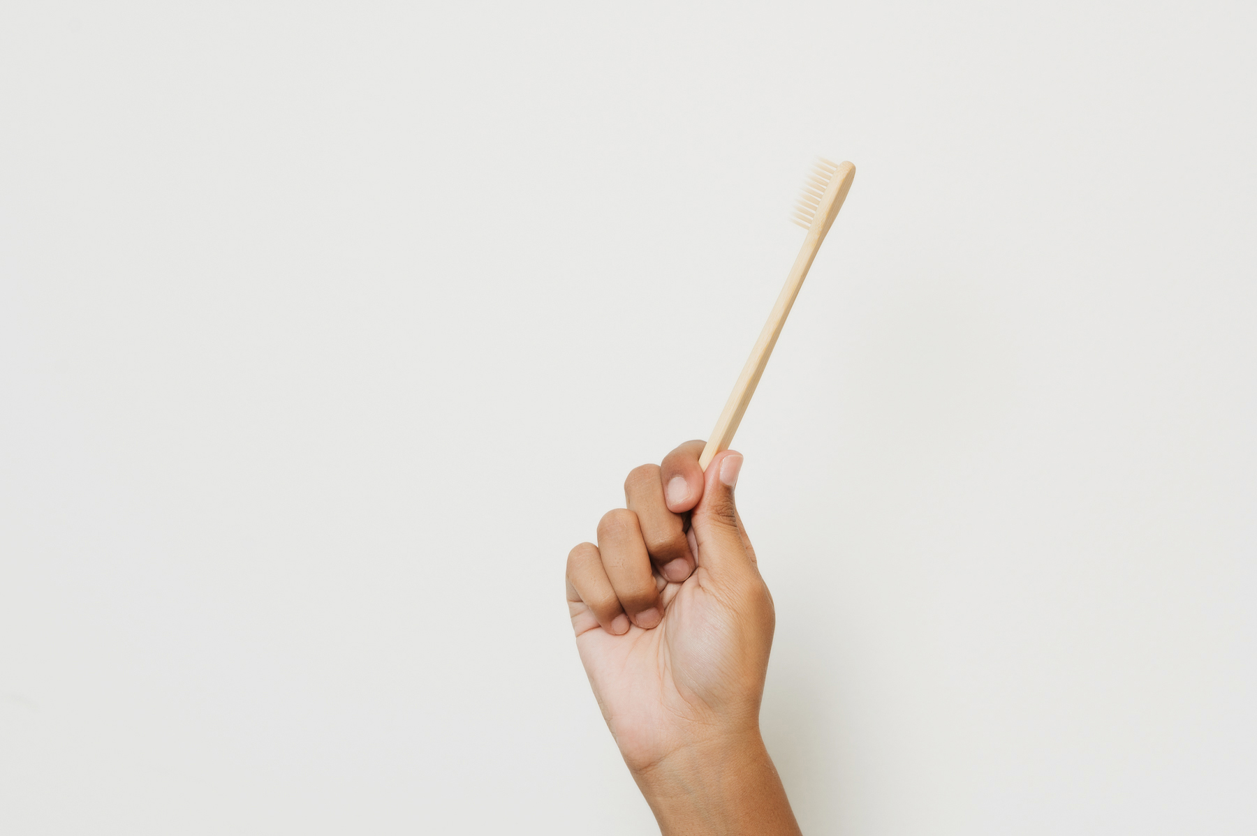 Hand holding a wooden toothbrush against a plain background