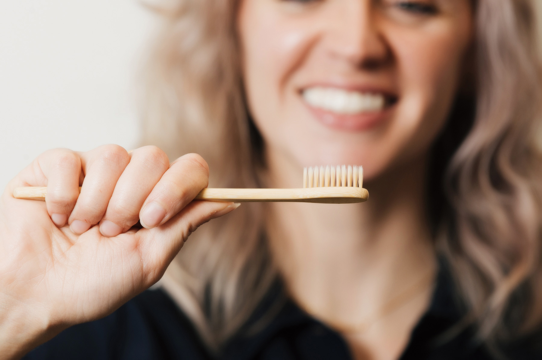 Smiling woman holding a wooden toothbrush close to the camera