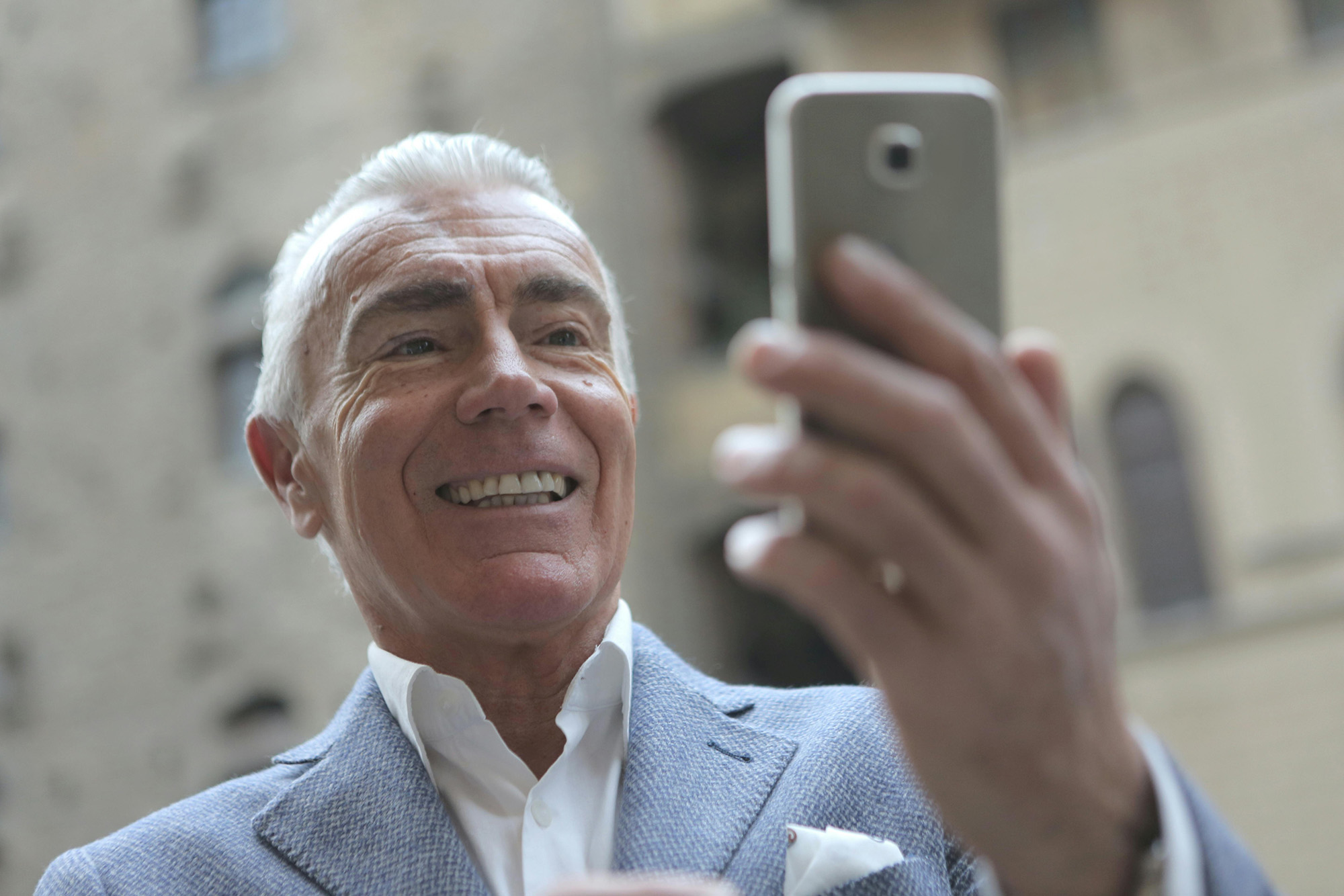 Smiling older man taking a photo with his phone outdoors