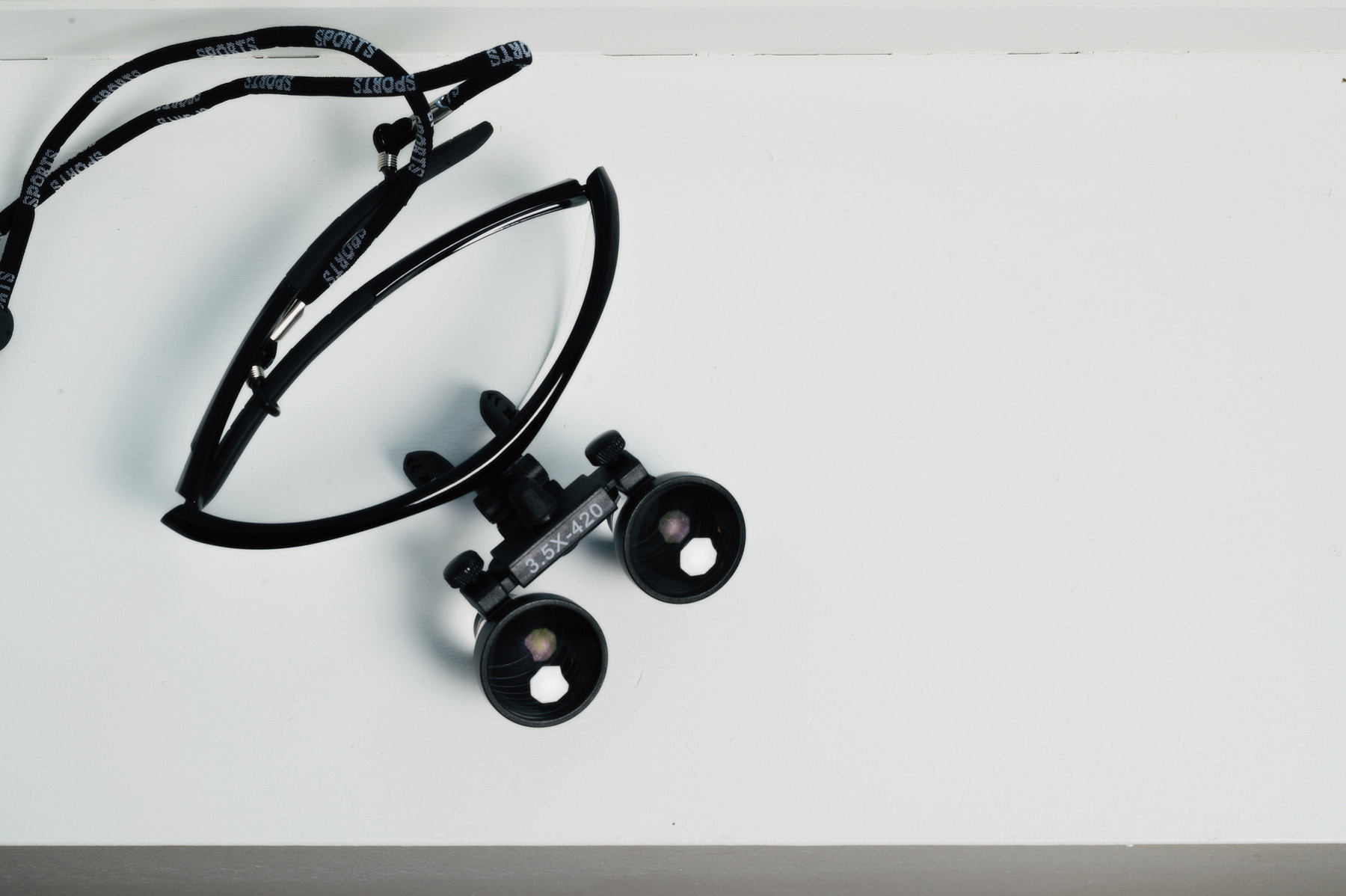 Pair of dental loupes with a sports strap resting on a white surface