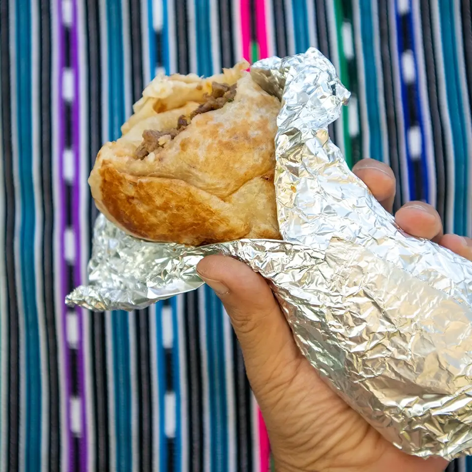 Hand holding a foil-wrapped burrito