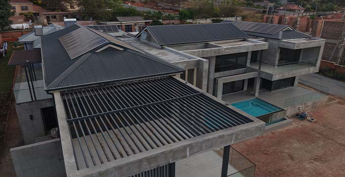 A modern luxury residential building with concrete and glass structure, featuring solar panels on the roof and a small outdoor pool next to the building.