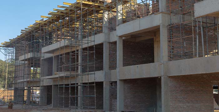 Multi-floor commercial building under construction with concrete beams, brick walls, and metal scaffolding against a clear blue sky.