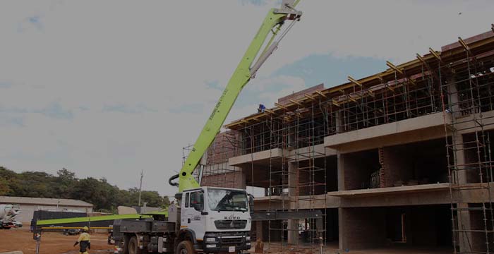 Construction site with a white crane truck with a raised green boom next to a multi-story building under construction with scaffolding and workers.