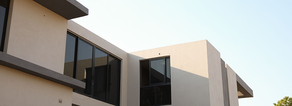 Modern beige building with large dark-tinted windows and angular concrete roof accents under a clear sky.