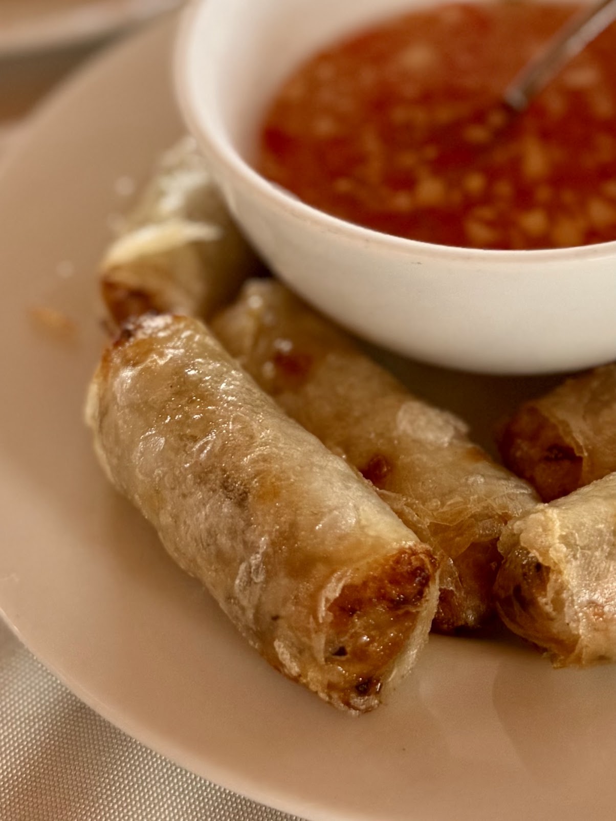 Fried lumpia on a white plate beside a small bowl of sweet chili dipping sauce