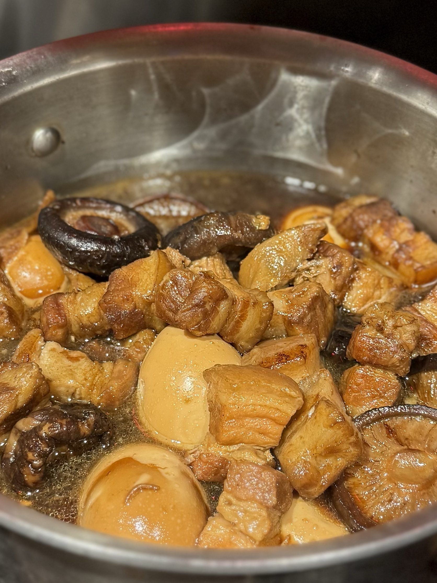Braised pork belly, shiitake and soy-browned eggs, glossy with sauce, in a stainless pot