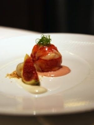 Butter-poached Maine lobster tail plated with a fig wedge, a pale cream sauce and a curl of chive on a wide white plate