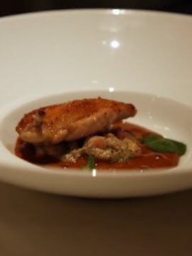 A small burnished quail breast resting on cranberry beans in a dark red-brown sauce, finished with a basil leaf