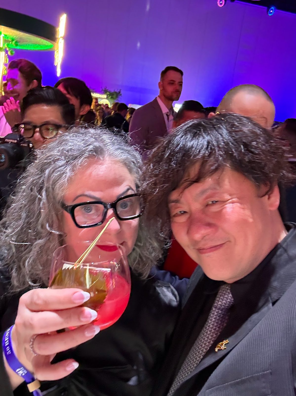Two guests at the reception, one holding up a red cocktail garnished with a cured leaf on a gold pick