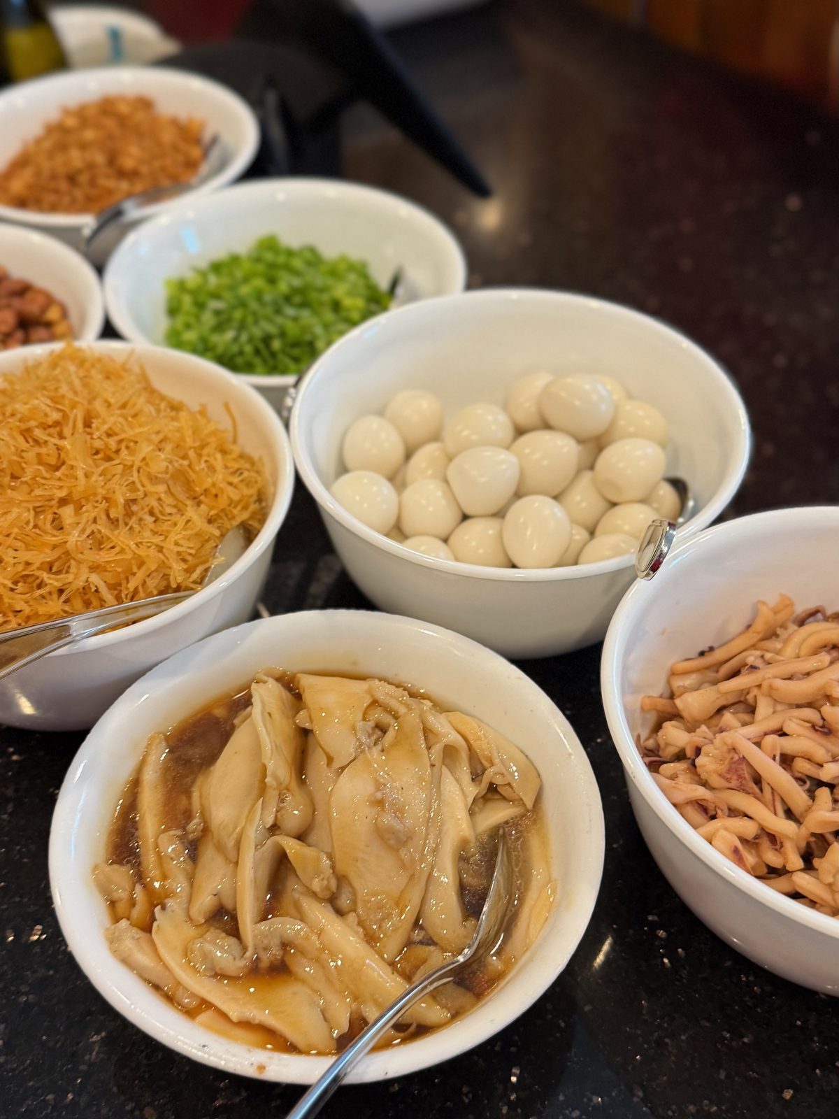 Bowls of separately cooked Tsa Misua toppings — shredded dried scallops, boiled quail eggs, abalone, cuttlefish, fried shallots, peanuts and chopped green onions