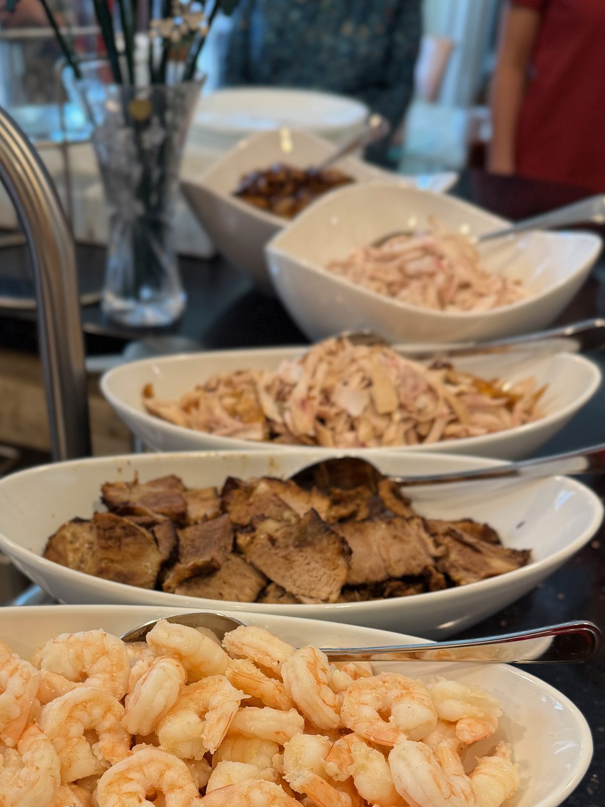 A line of serving bowls along the kitchen counter — shrimp, braised pork shoulder and shredded soya chicken