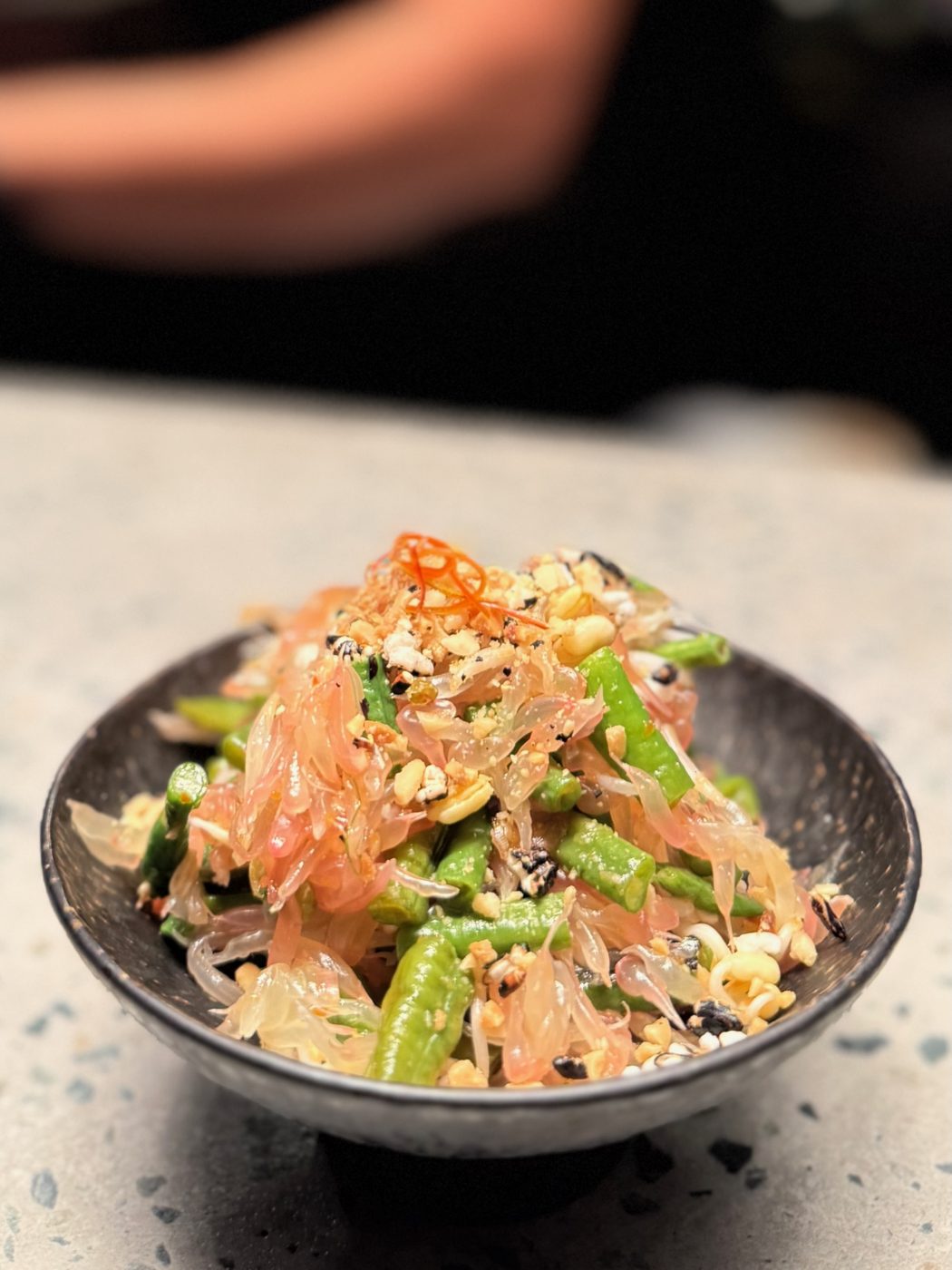 Som Tam in a dark bowl — shredded green papaya and pomelo segments tossed with snake beans, crushed peanuts and slivered red chili