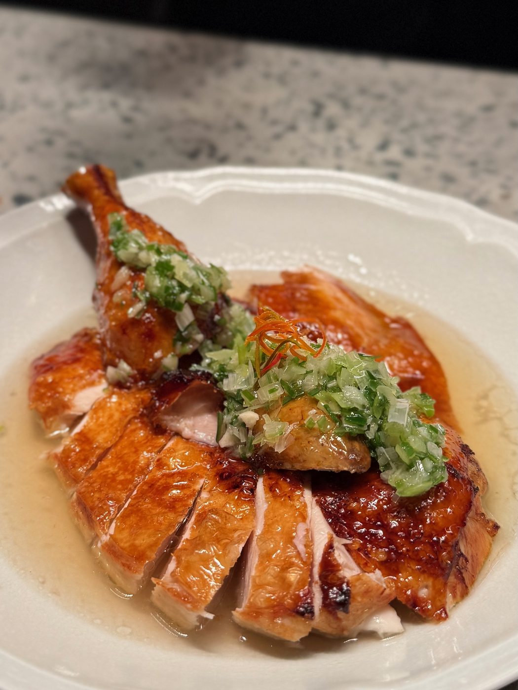 Shan Tung Chicken — half a bird sliced and fanned out, skin glazed mahogany, under a raw scatter of spring onion and ginger in a pale broth