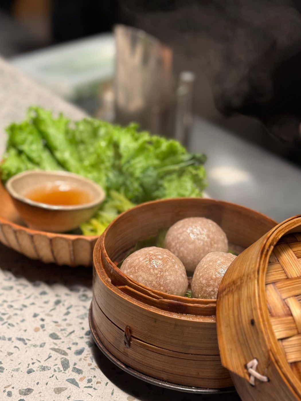 Pork and XO dumplings in a bamboo steamer, with lettuce leaves and a small bowl of sweet vinegar dipping sauce alongside
