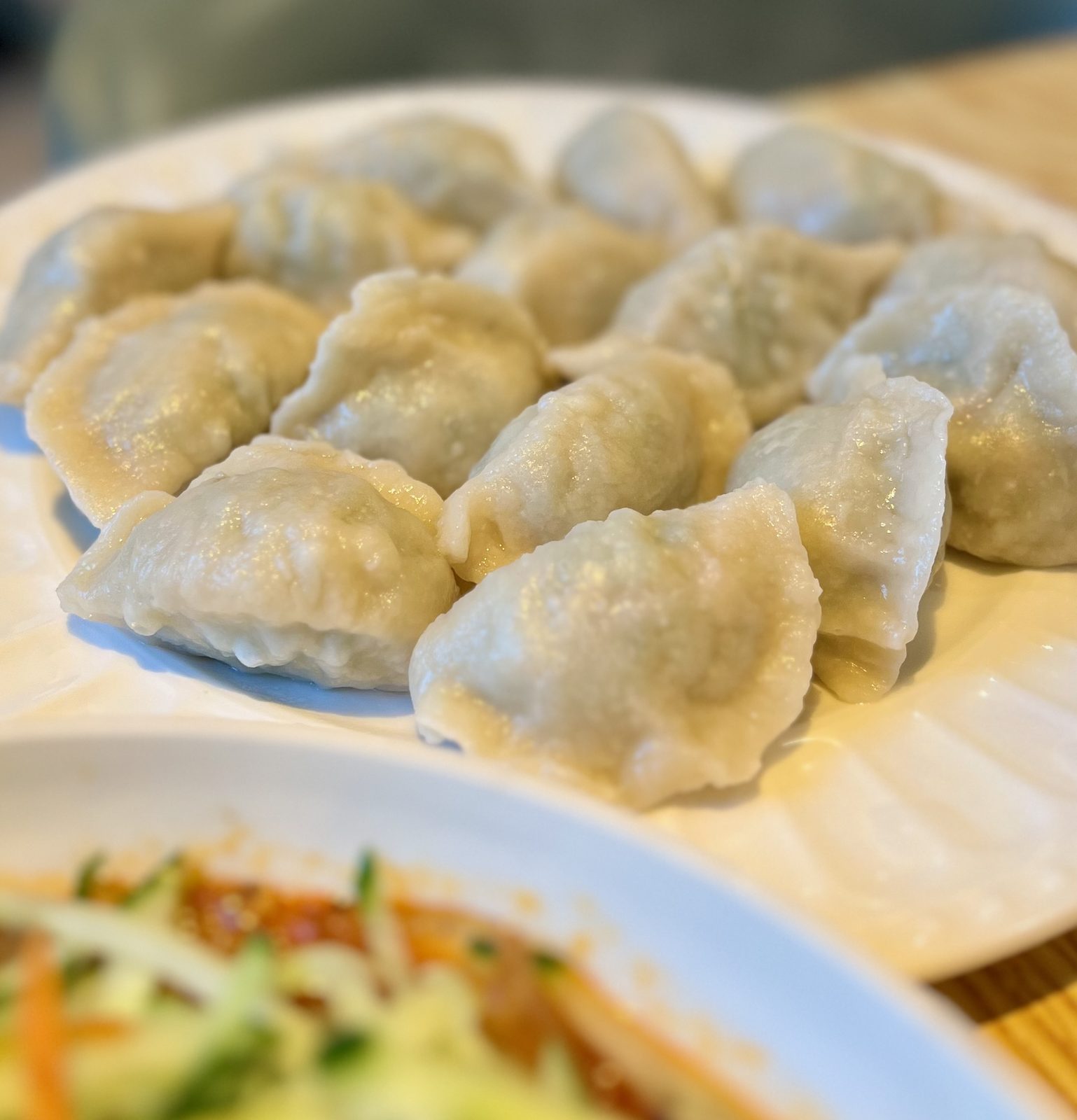 A plate of boiled jiaozi, pleated crescents glistening and packed close together, with a dish of shredded cold vegetables in the foreground