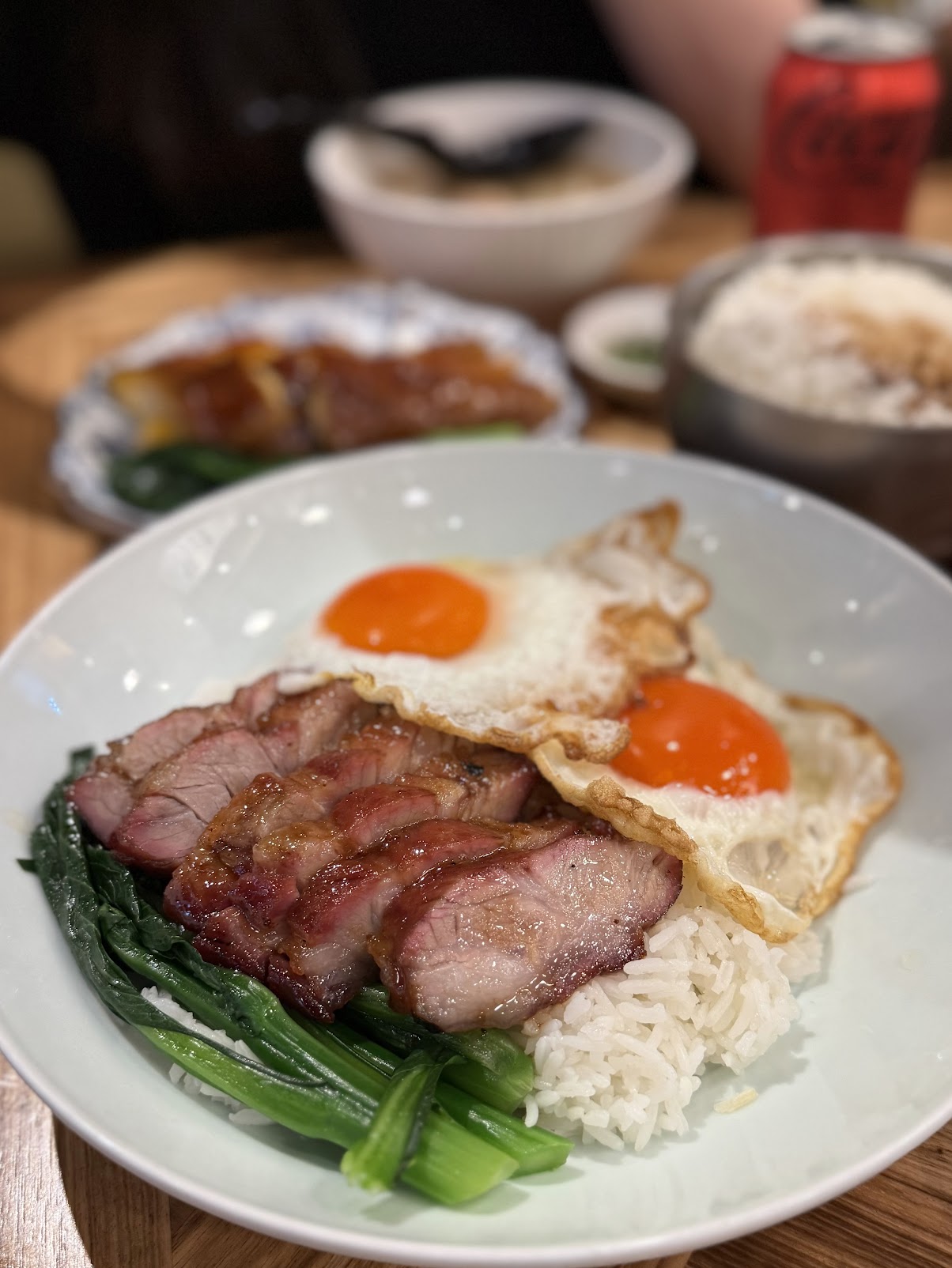 Sliced char siu over rice with two fried eggs, their yolks still soft, and a bed of gai lan alongside