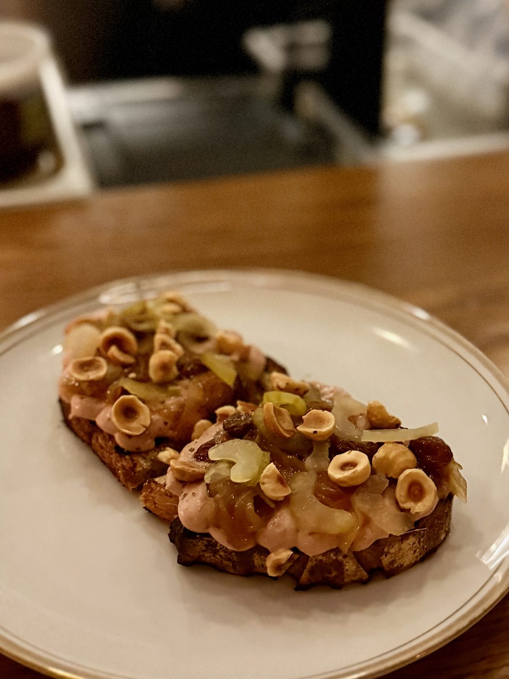 Dark-grilled sourdough spread with pale chicken liver parfait, topped with halved toasted hazelnuts, golden raisins and slices of pale celery