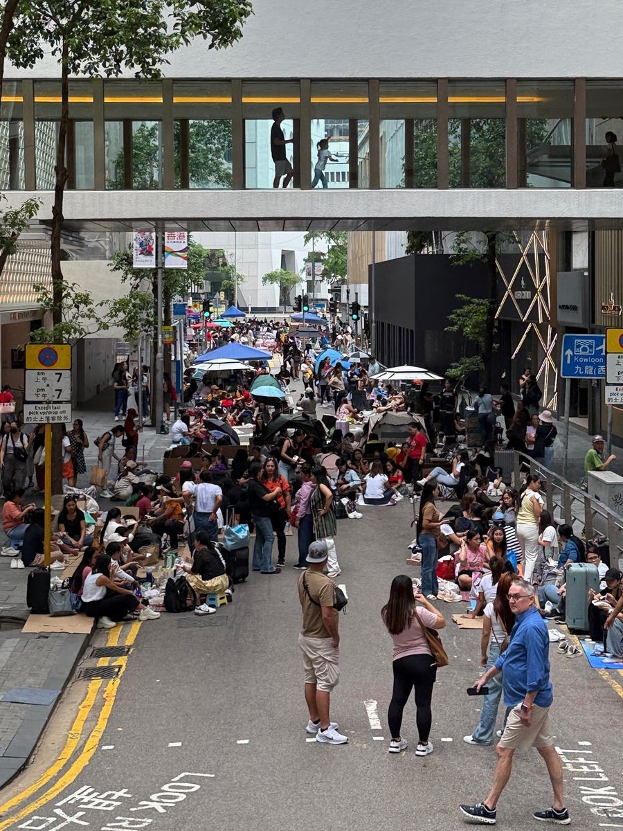 Hundreds of people gathered on a closed street in Central, Hong Kong on a Sunday, sitting on flattened cardboard under umbrellas