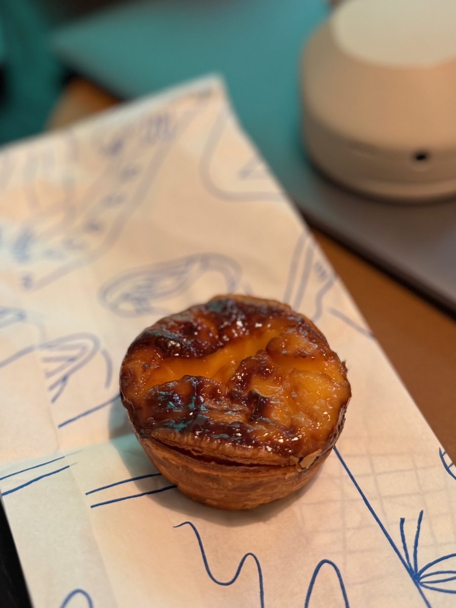 A single sourdough egg tart on its printed paper wrapper, the top lightly caramelized