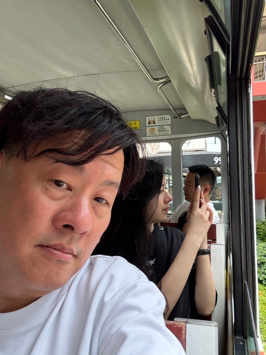 The upper deck of a Hong Kong double-decker tram with the windows open and the street passing outside