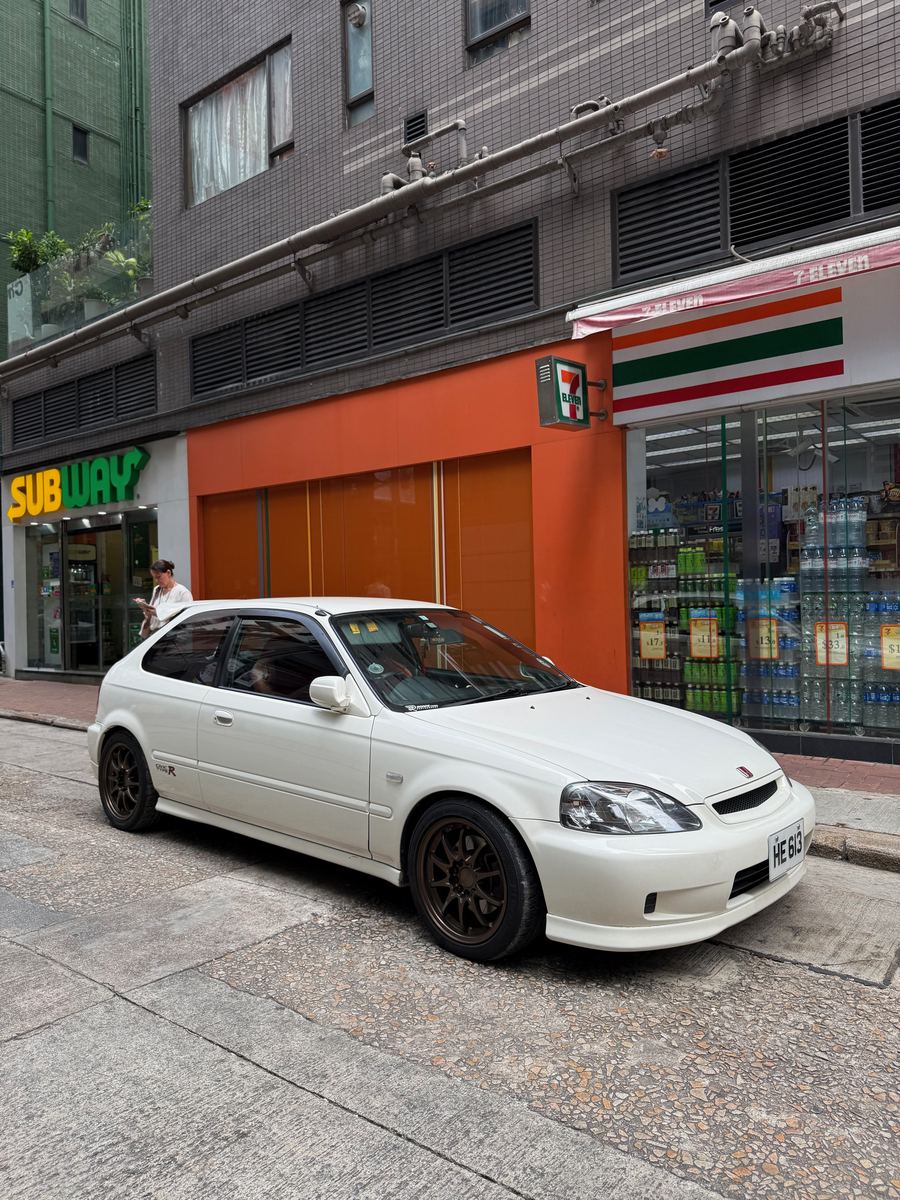 A white Honda Civic EK9 Type R parked on a Hong Kong street outside a convenience store