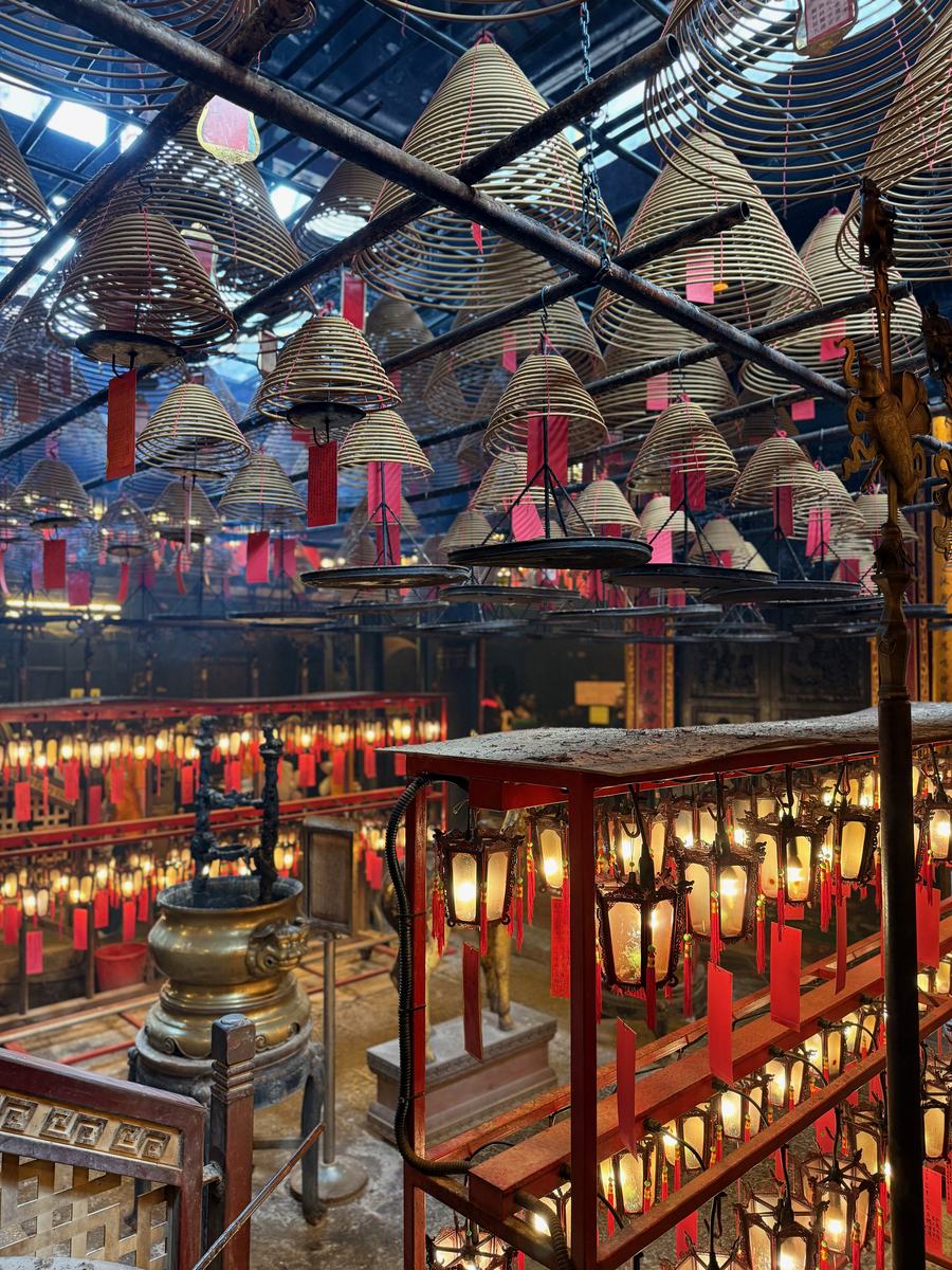 Large spiral incense coils hanging from the ceiling of Man Mo Temple in Hong Kong among red lanterns
