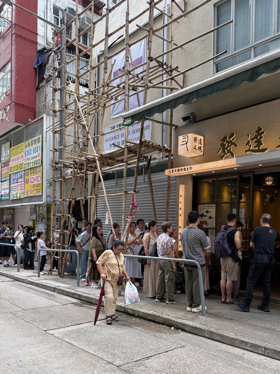 A queue along the pavement outside a Hong Kong roast meat shop, under bamboo scaffolding