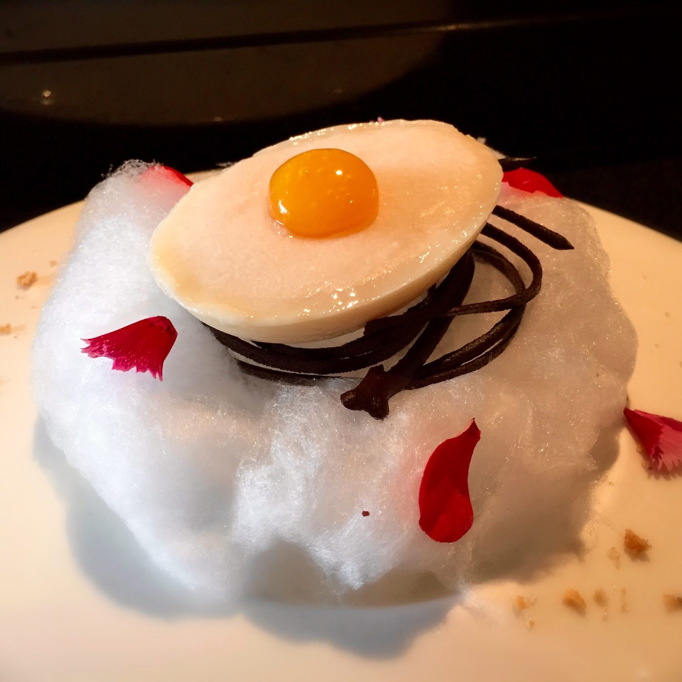 A dessert built to look like a fried egg: white chocolate over chirimoya for the white, goldenberry gel for the yolk, with a cacao nest and cotton candy.