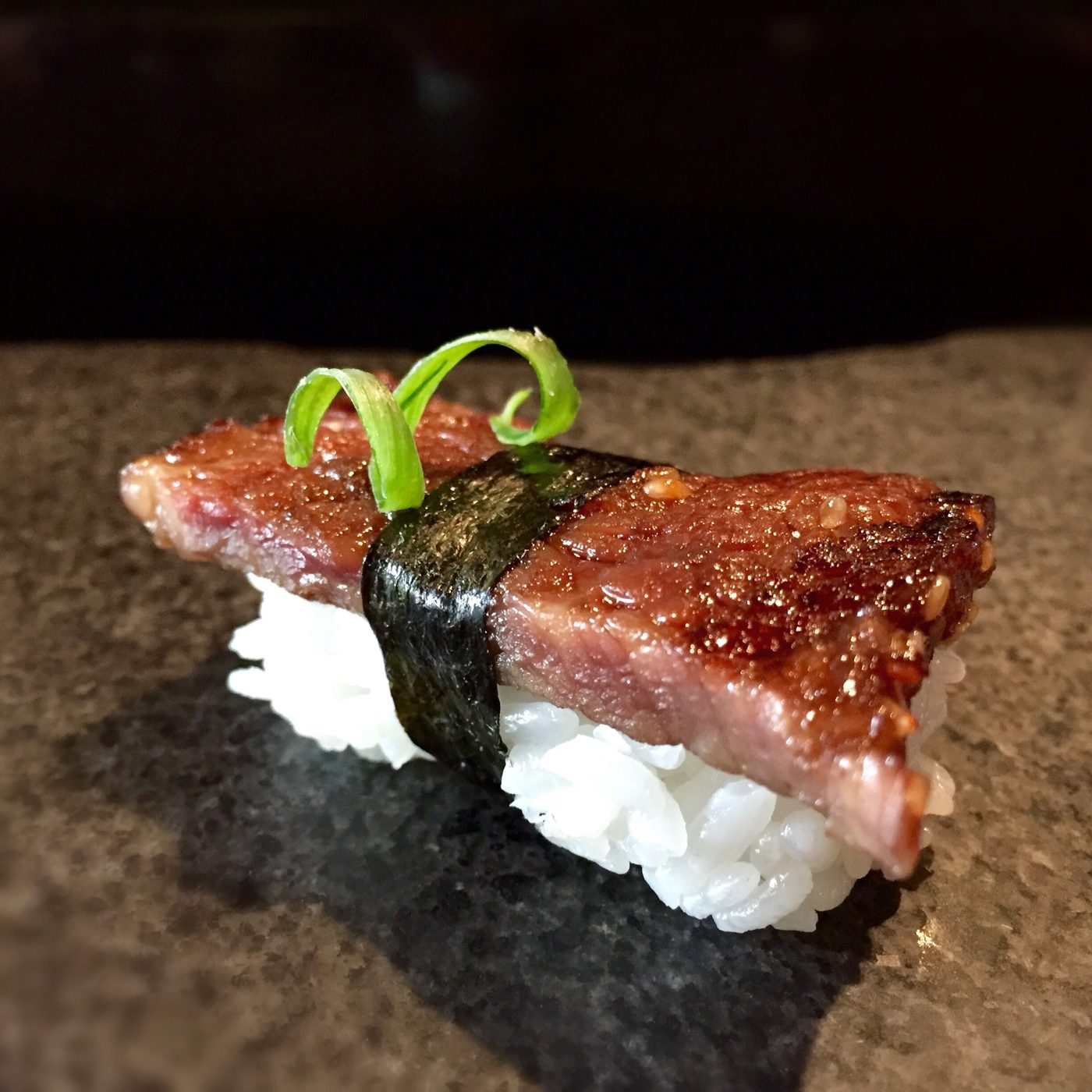 A thick slab of lacquered short rib scattered with sesame on sushi rice, banded with nori and topped with two curls of scallion.