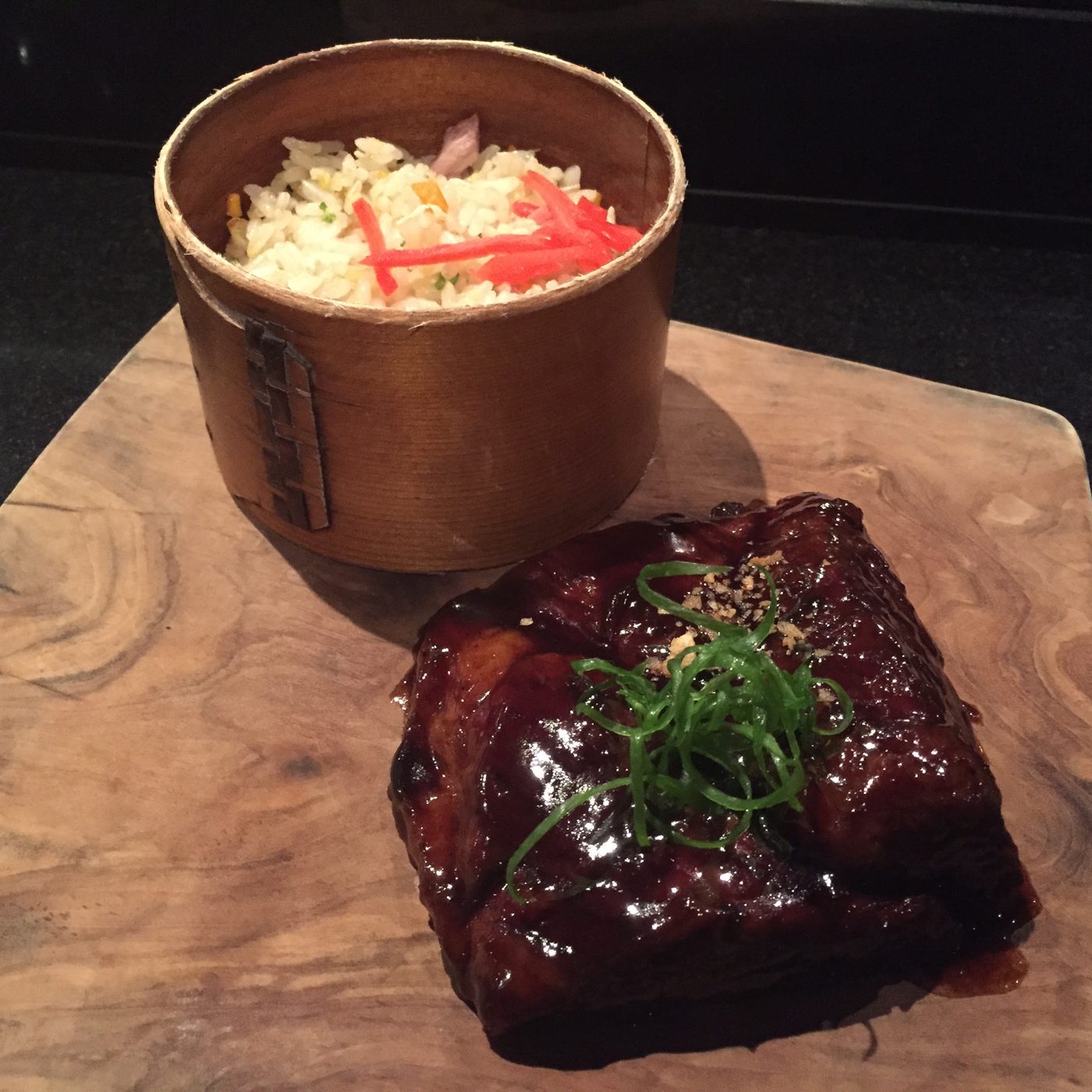 A dark-lacquered block of beef short rib cooked for fifty hours, with a bamboo box of fried rice beside it.