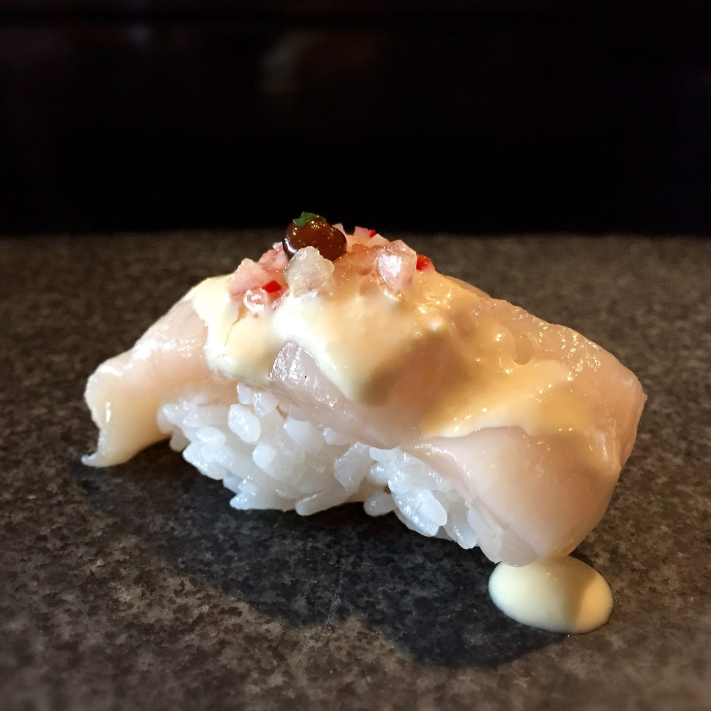 A nigiri of thick white scallop under a pale cream sauce scattered with pink-red flecks.