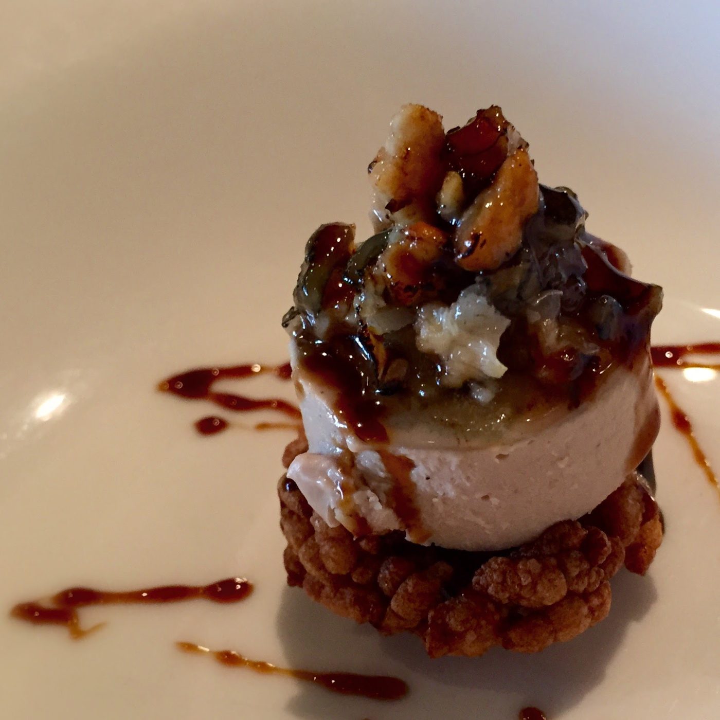 A cratered deep-fried puffed-rice disc topped with pale mousse and a pile of glazed seafood and greens, with glaze flicked across the plate.