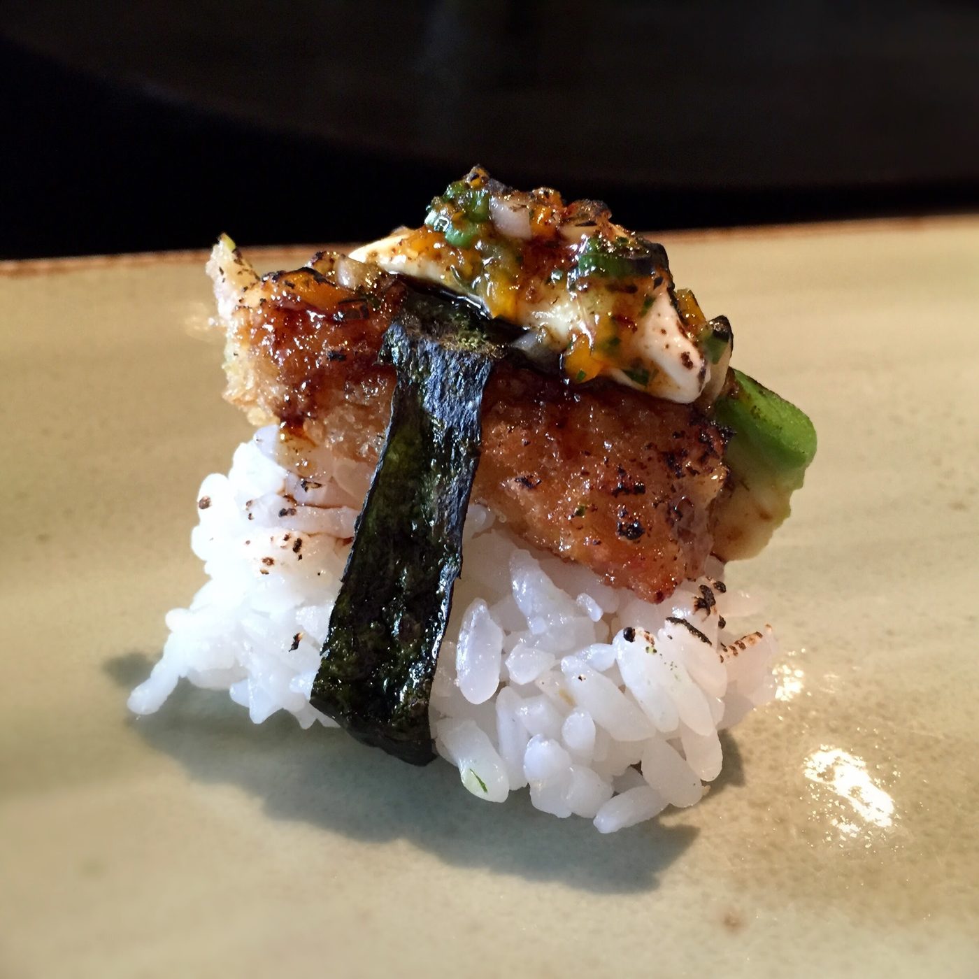 A nigiri banded with nori, its top browned and torched, finished with green salsa and scallion.