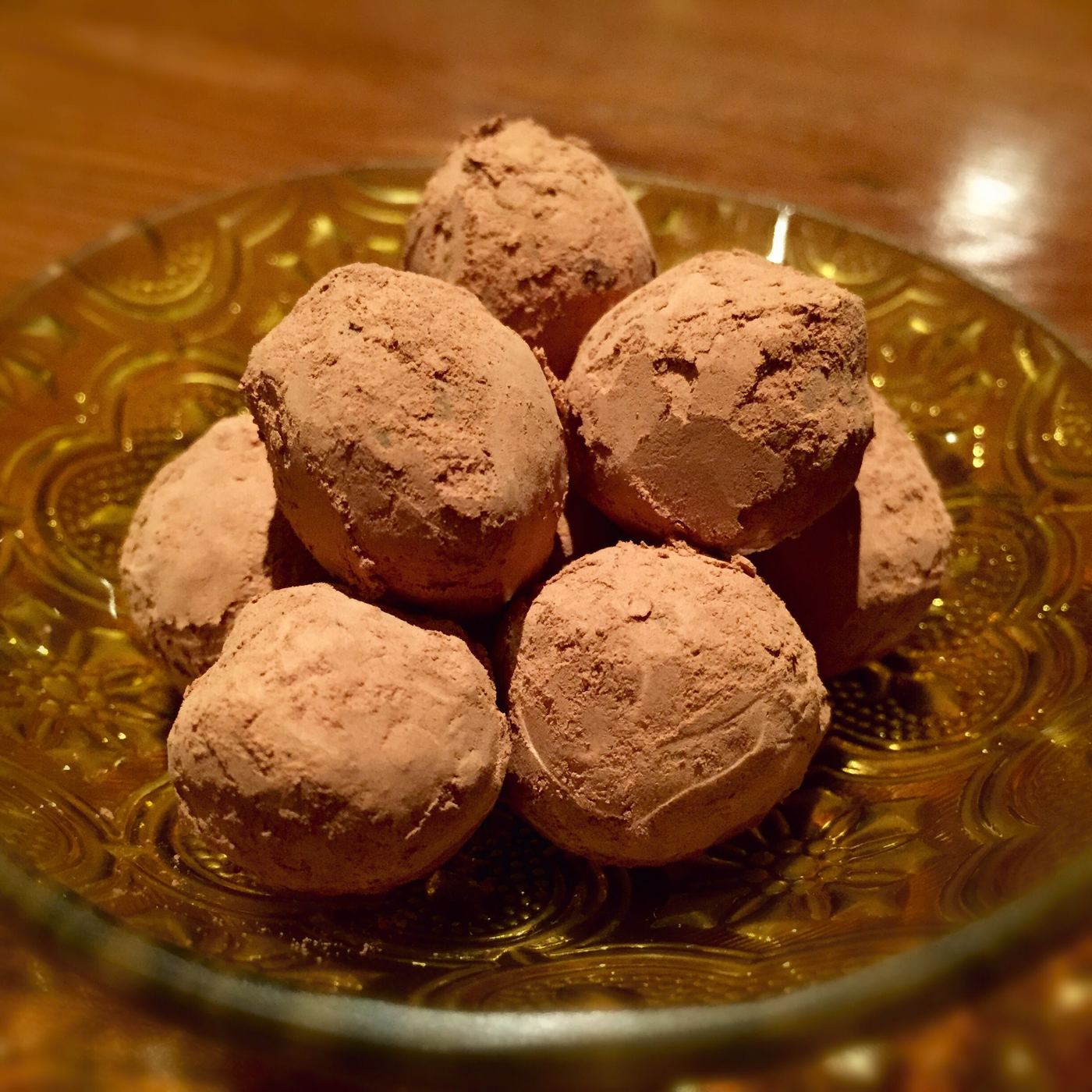 Seven rough spheres piled on a pressed amber glass dish, each thickly dusted in cocoa with the dark shell showing through where the dusting has rubbed off.