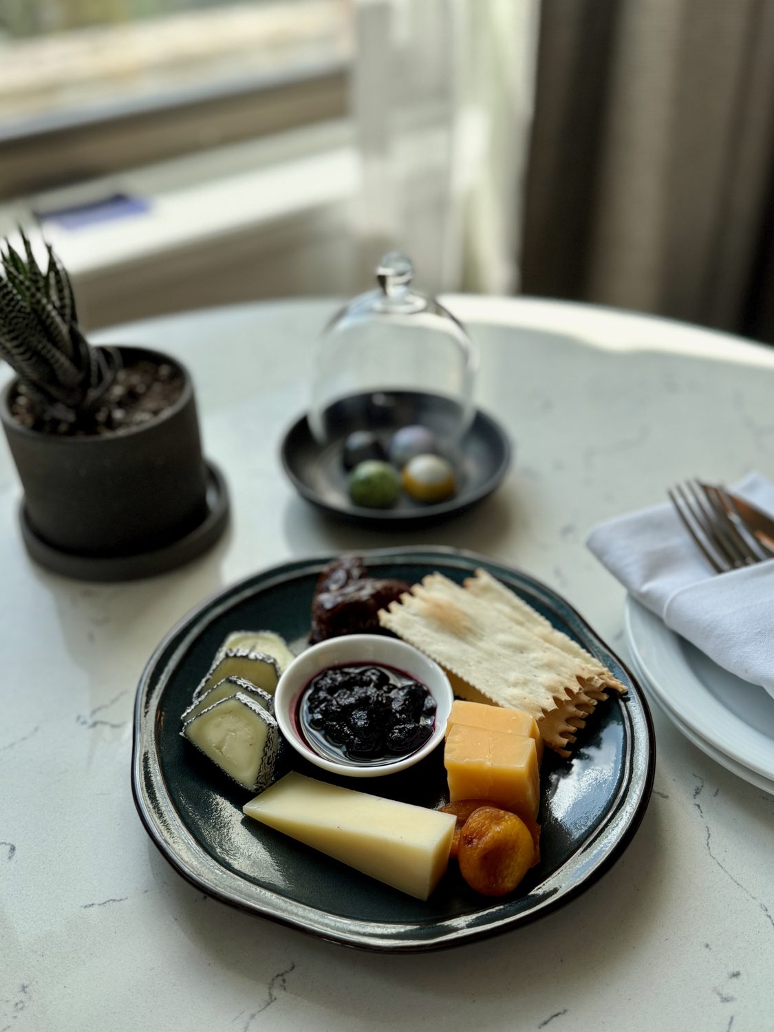 A welcome plate of cheeses with compote, dried apricot and lavash, beside chocolate bonbons under a glass cloche