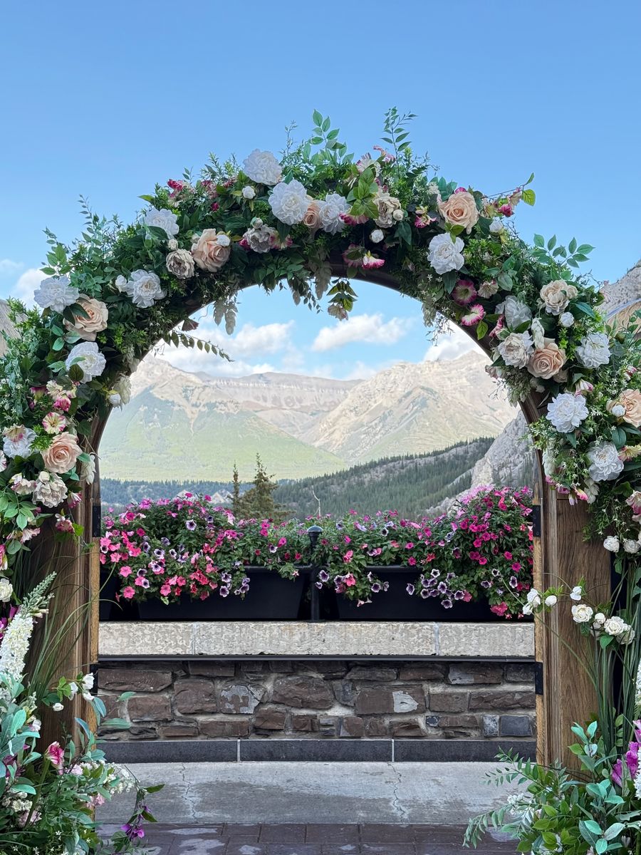 A wedding arch dressed in roses and greenery on a hotel terrace, framing the mountains beyond