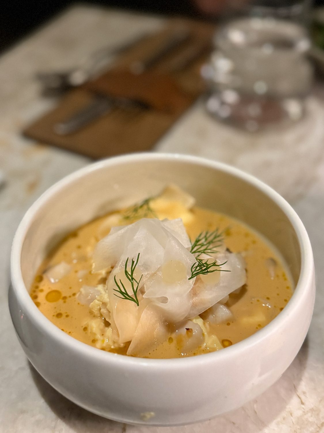 White fish in a golden broken-cream broth beaded with orange oil, under translucent shavings of daikon and sprigs of dill