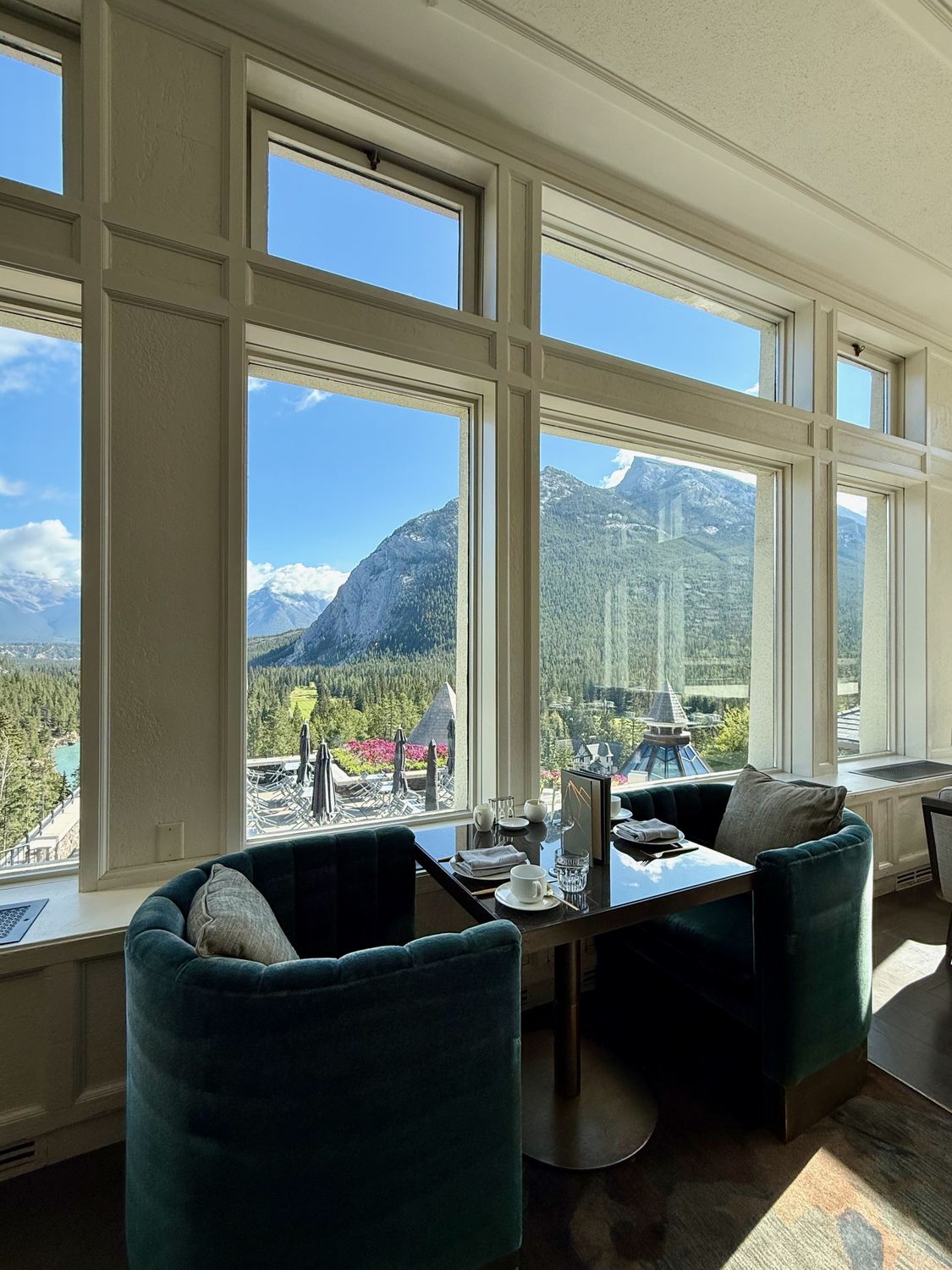 A window table set for afternoon tea, looking out over the Bow River, the hotel terrace and the mountains beyond